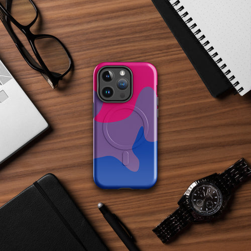 Phone case with pink and blue design on a wooden desk with glasses, laptop, and watch.