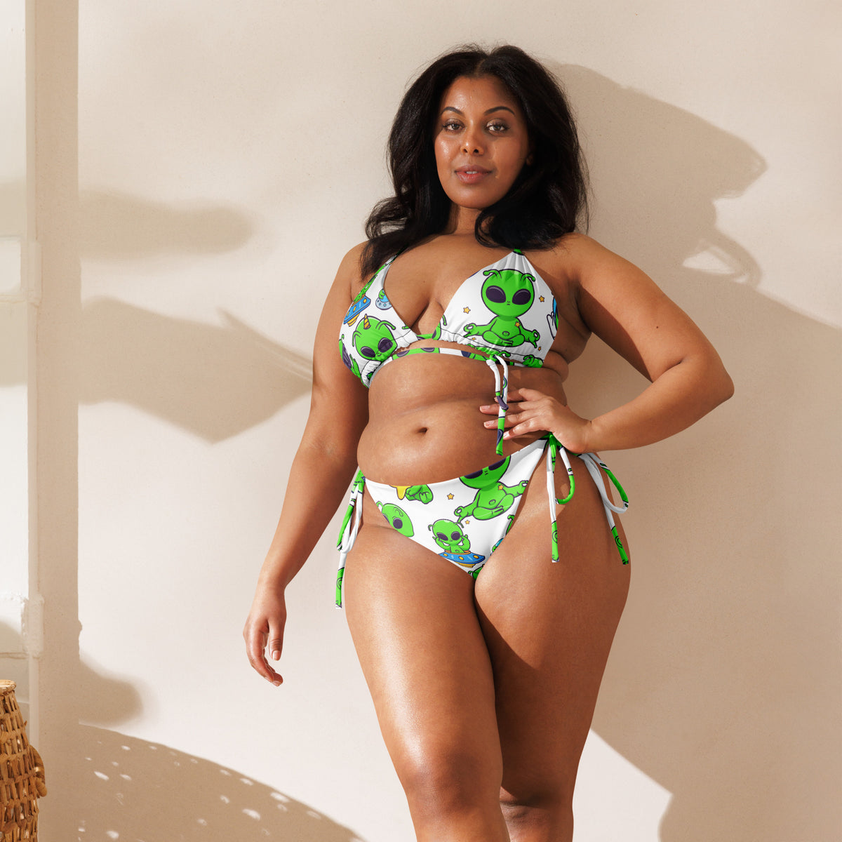 Woman wearing a green and white bikini with alien design against a neutral background
