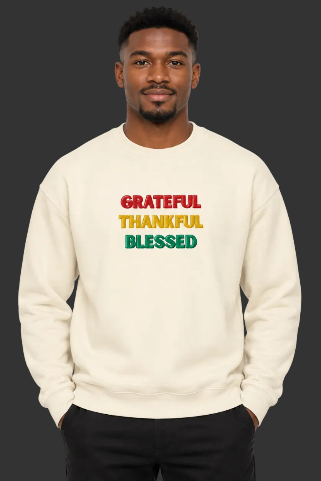 A cream-colored crewneck sweatshirt with the words 'GRATEFUL', 'THANKFUL', and 'BLESSED' printed on the chest in red, yellow, and green block letters, shown against a plain white background.