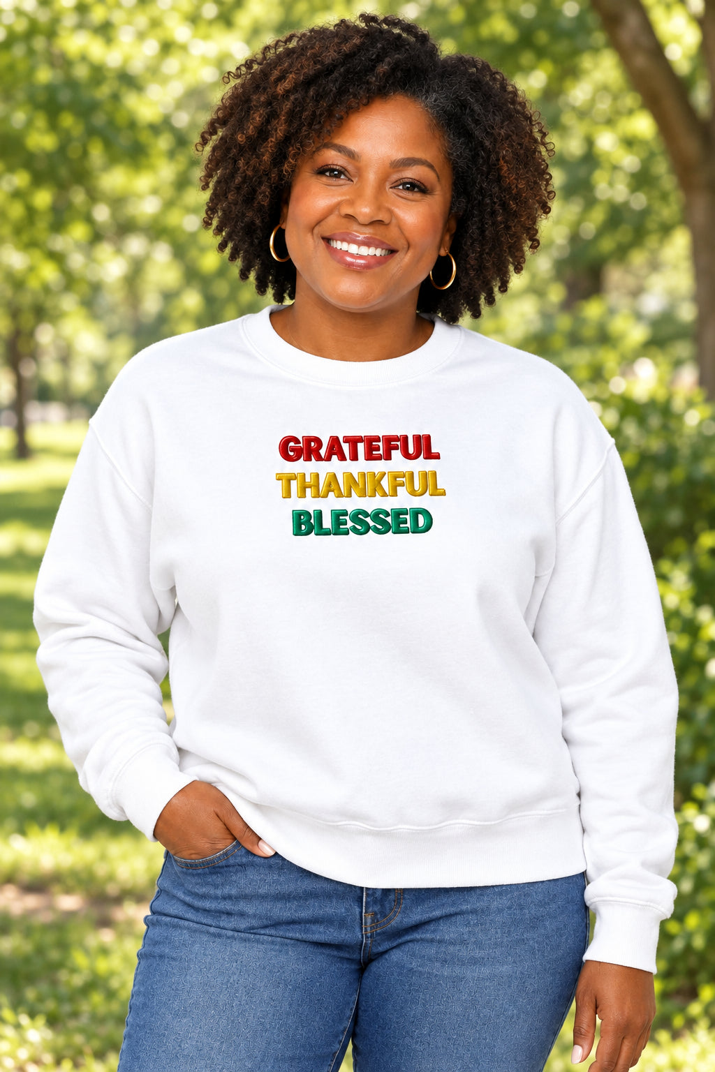 A white crewneck sweatshirt featuring the words 'GRATEFUL', 'THANKFUL', and 'BLESSED' printed vertically on the chest in red, yellow, and green, respectively.