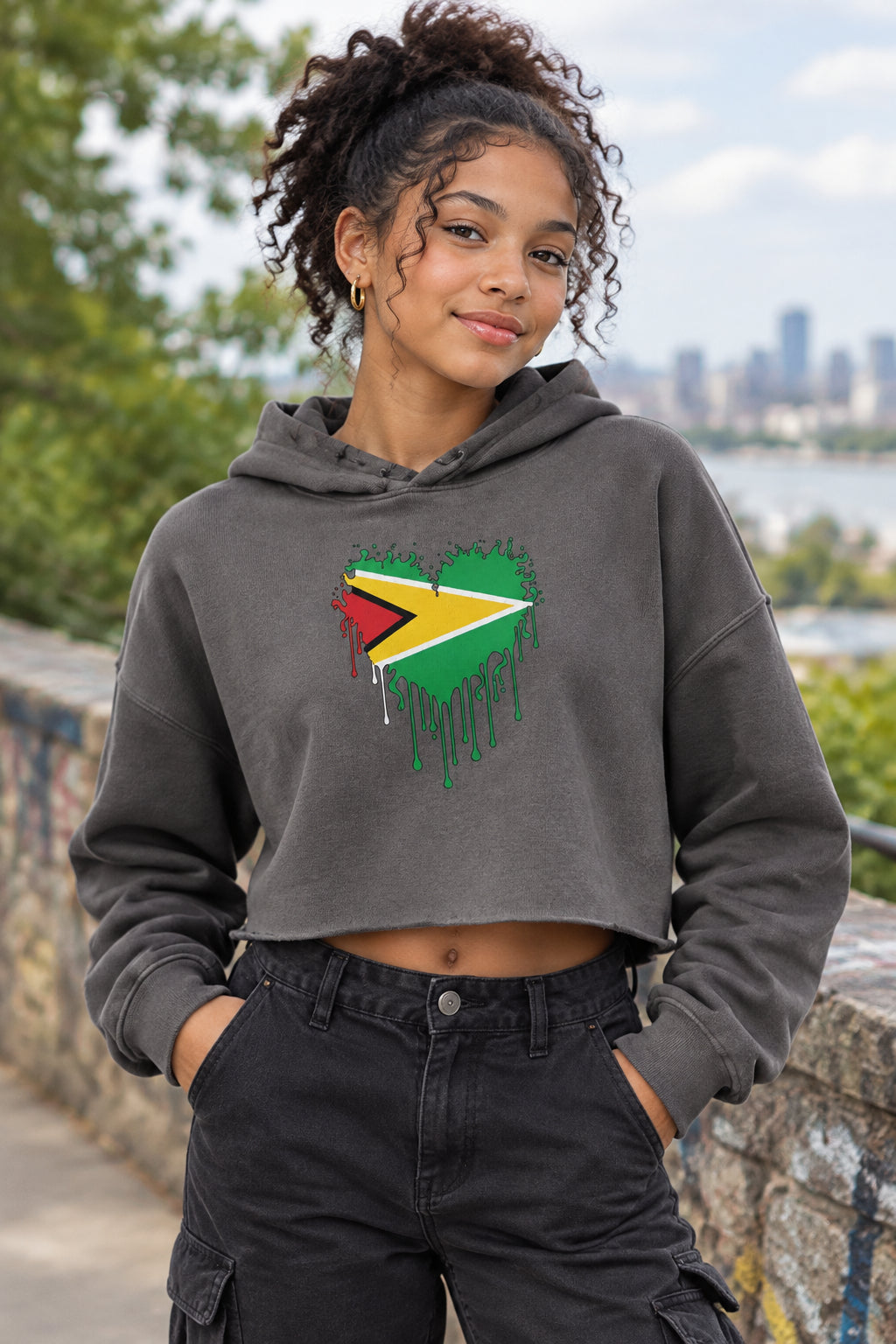 A grey cropped hoodie with a graphic of the Guyana flag forming a heart shape on the chest, with a dripping paint effect. The hoodie is shown against a plain white background.