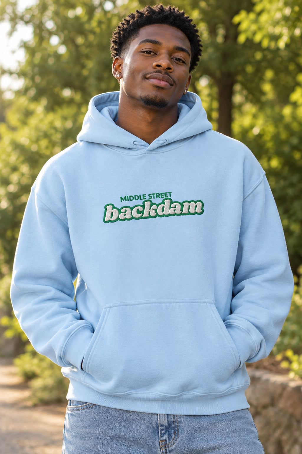 A light blue pullover hoodie with a front kangaroo pocket and a chest graphic reading 'MIDDLE STREET backdam' in green and white, shown on a plain white background.