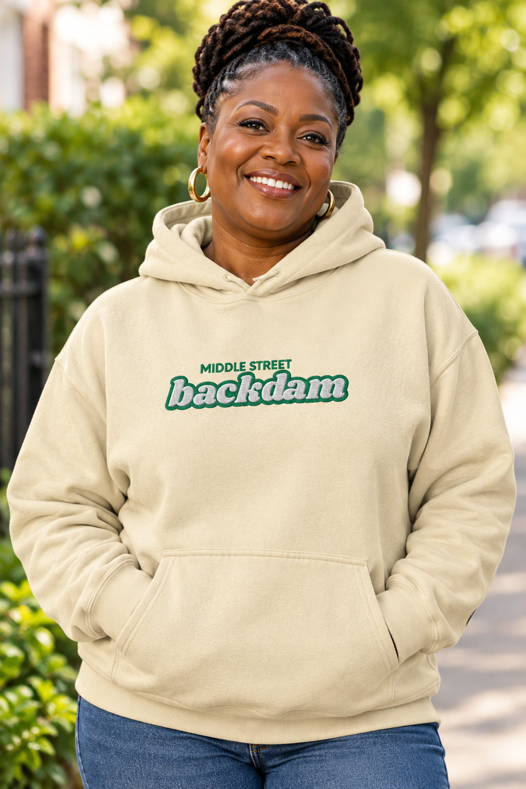 A light beige pullover hoodie with a front kangaroo pocket and a chest graphic reading 'MIDDLE STREET backdam' in green and white. The hoodie is shown against a plain white background.