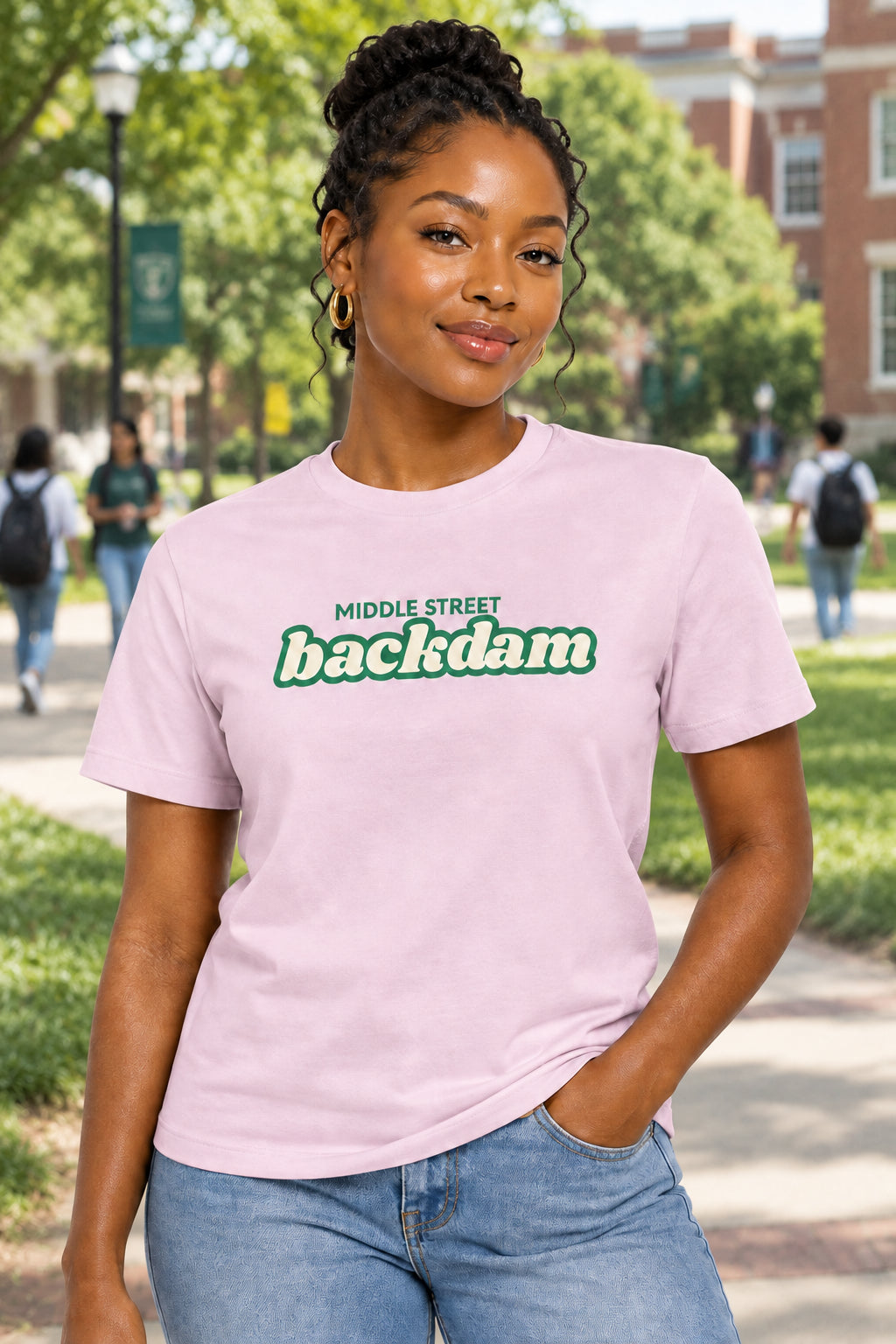 A light pink short-sleeve crewneck t-shirt with a green and white graphic text print reading 'MIDDLE STREET backdam' on the chest, displayed against a solid white background.