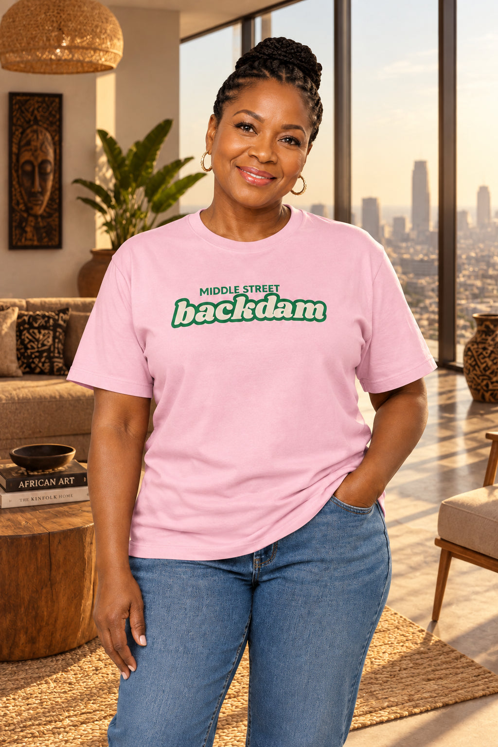 A light pink short-sleeve crewneck t-shirt with a green graphic text print reading 'MIDDLE STREET backdam' across the chest, displayed on a clean white background.