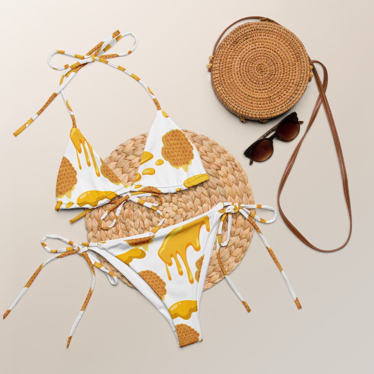 Bikini set with yellow and white pattern, straw hat, round woven bag, and sunglasses on a beige background